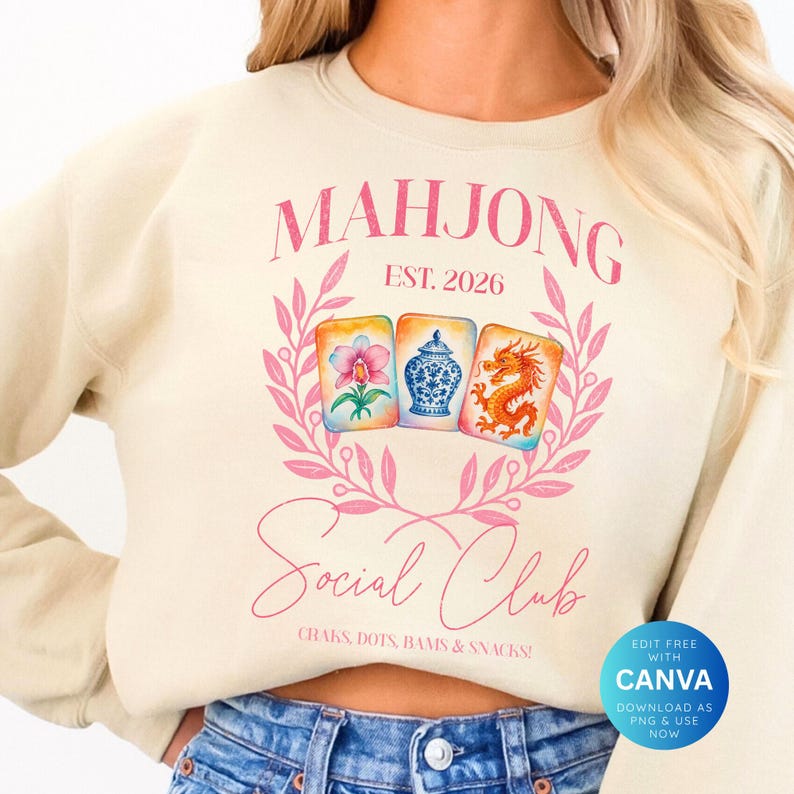 May include: Cream-colored sweatshirt with a pink floral design and the words "MAHJONG Social Club" in pink script. The design includes three illustrated Mahjong tiles and the text "EST. 2026". The phrase "CRAKS, DOTS, BAMS & SNACKS!" is also included.