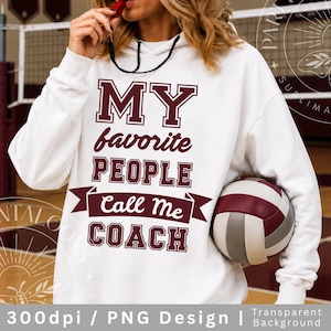 Może przedstawiać: Biała bluza z kapturem z napisem "MY favorite PEOPLE Call Me COACH" w kolorze bordowym. Piłka do siatkówki z bordowymi i szarymi panelami trzymana jest w prawym ramieniu. Gwizdek trzymany jest w ustach.