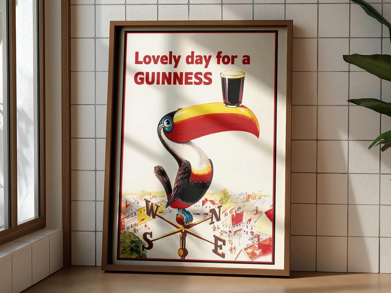 May include: Framed vintage Guinness advertisement featuring a toucan with a large yellow, red, and black beak, holding a pint of Guinness. The text reads "Lovely day for a Guinness." The artwork is set against a cream background.