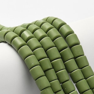 Può includere: Una collana di perline in ceramica verde, ogni perlina è cilindrica e ha una finitura opaca. Le perline sono disposte a scalare, creando una texture visivamente accattivante.
