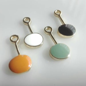 May include: Four gold-colored metal charms with different colored enamel circles. The circles are white, black, green, and orange.