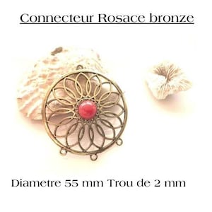 Puede incluir: Un conector de metal de color bronce con una pieza central roja y un diseño decorativo. El conector tiene un diámetro de 55 mm y un agujero de 2 mm.