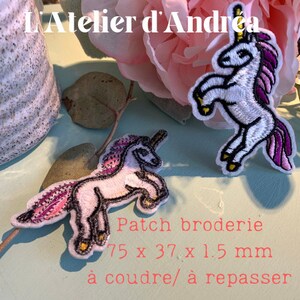 May include: Embroidered unicorn patches with pink and purple manes and tails. The patches are white with black outlines and gold accents. The text "L'Atelier d'Andrea" is at the top. The patches measure 75 x 37 x 1.5 mm.
