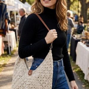 May include: A beige crochet hobo bag featuring a textured, open-weave pattern, a single brown leather-like strap, and a small brown tab closure with a gold-tone metal snap button at the center of the top opening.