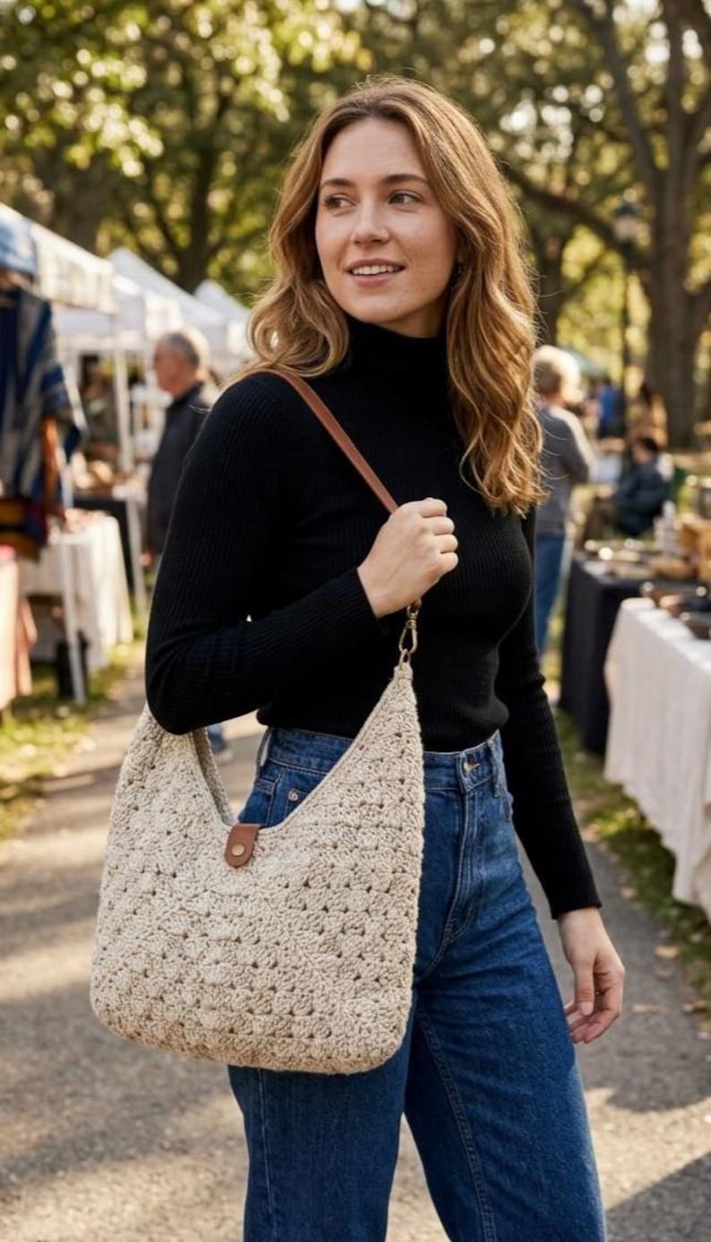 May include: A beige crochet hobo bag featuring a textured, open-weave pattern, a single brown leather-like strap, and a small brown tab closure with a gold-tone metal snap button at the center of the top opening.
