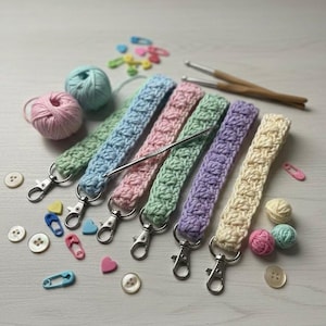 May include: Six pastel-coloured crochet wrist straps, each with a silver clasp. The colours are green, blue, pink, green, purple, and cream. The image also shows balls of yarn, buttons, safety pins, and crochet hooks.