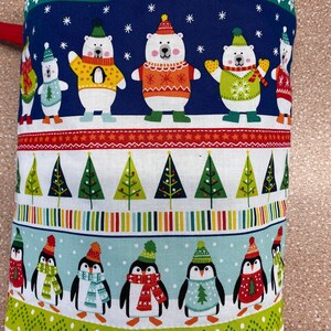 May include: A blue and white fabric with a repeating pattern of penguins and polar bears wearing festive hats and jumpers. The fabric features a red, white and green striped border with a repeating pattern of Christmas trees.