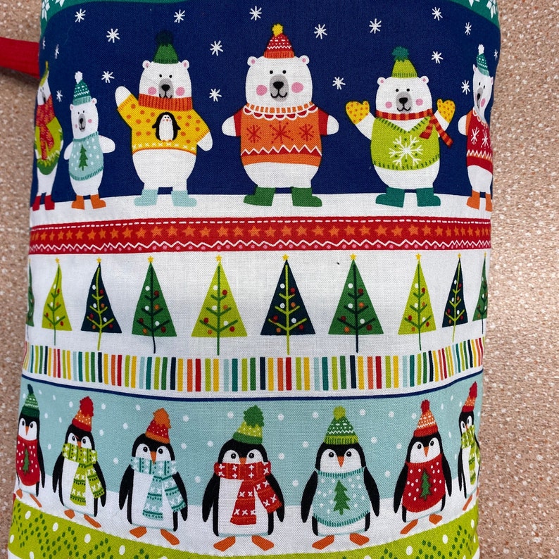 May include: A blue and white fabric with a repeating pattern of penguins and polar bears wearing festive hats and jumpers. The fabric features a red, white and green striped border with a repeating pattern of Christmas trees.