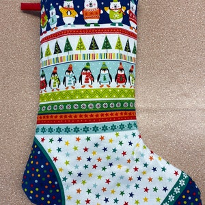Peut inclure: Une chaussette de Noël avec un fond bleu et une variété de motifs colorés. La chaussette représente des pingouins, des ours polaires et des flocons de neige. Le bout de la chaussette est un motif de pois bleus et verts.
