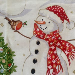 May include: A festive fabric featuring snowmen with black button eyes, carrot noses, and red and white polka-dot hats and scarves. A small bird with a sprig of holly sits on a branch near a snowman. A Christmas tree is also visible.