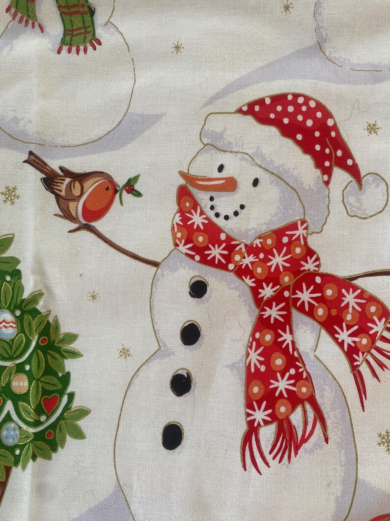 May include: A festive fabric featuring snowmen with black button eyes, carrot noses, and red and white polka-dot hats and scarves. A small bird with a sprig of holly sits on a branch near a snowman. A Christmas tree is also visible.