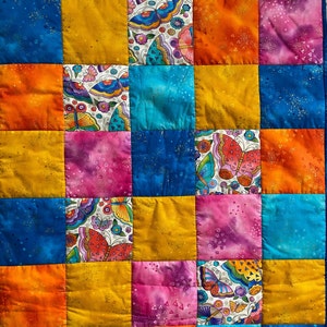 Peut inclure: Une courtepointe colorée en patchwork avec un motif de carrés répétés. Les carrés sont dans des tons de bleu, orange, jaune et rose. Certains carrés présentent des motifs de papillons sur fond blanc. La courtepointe est cousue à la machine.