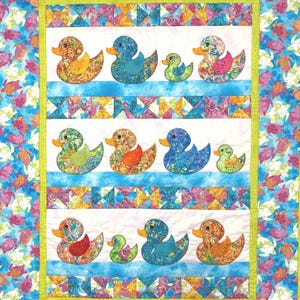 以下が含まれることがあります： 青、オレンジ、緑など、さまざまな模様と色でアップリケされたアヒルのカラフルなキルト。キルトは、青いストライプの白い背景と、カメと幾何学模様のボーダーがあります。全体的なデザインは明るく陽気です。