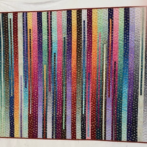 以下が含まれることがあります： 様々な色と模様の縦縞が施されたカラフルなキルト。キルトは、質感のある表面の生地で作られており、赤、オレンジ、黄色、緑、青、紫、茶色など、さまざまな色を使用しています。