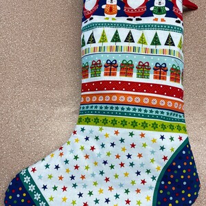 May include: A Christmas stocking with a white background and a variety of colourful patterns, including stars, stripes, snowflakes, and Christmas trees. The stocking features a blue cuff with white snowflakes and a red cuff with white polka dots. The stocking is decorated with images of Father Christmas, polar bears, and presents.