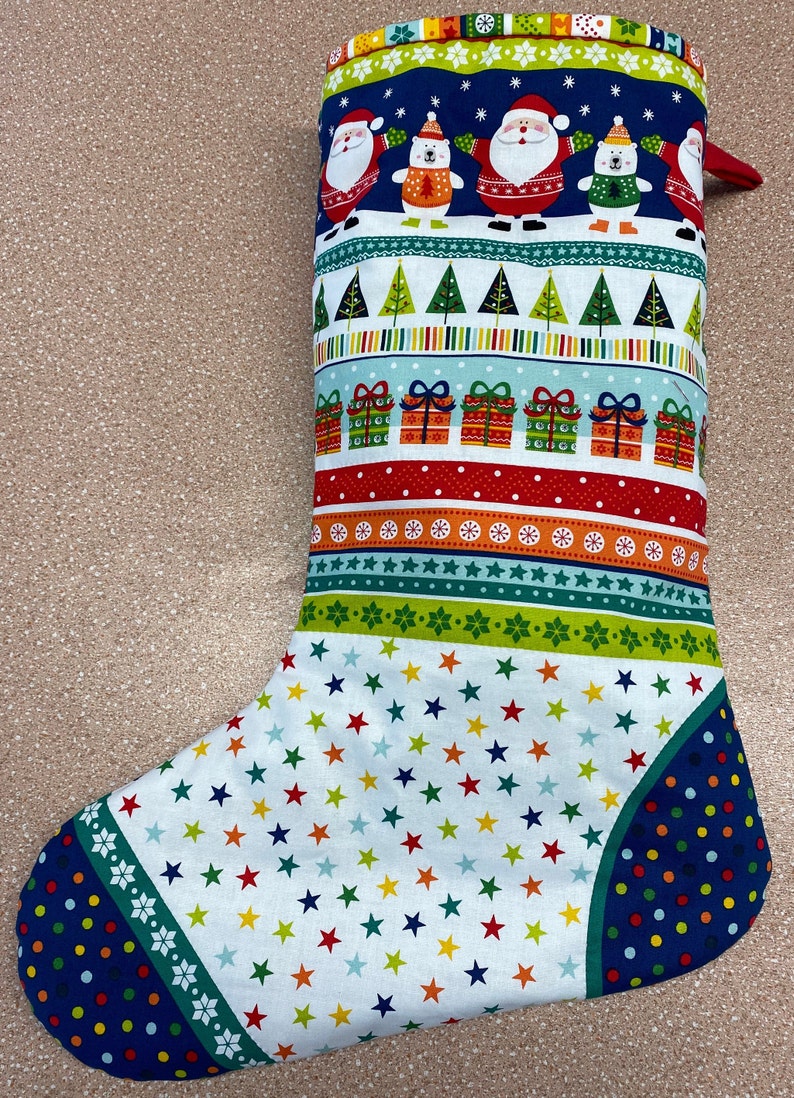 May include: A Christmas stocking with a white background and a variety of colourful patterns, including stars, stripes, snowflakes, and Christmas trees. The stocking features a blue cuff with white snowflakes and a red cuff with white polka dots. The stocking is decorated with images of Father Christmas, polar bears, and presents.