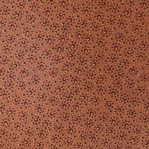 Può includere: Un primo piano di un tessuto marrone con un motivo ripetitivo di piccoli cerchi marroni scuri su uno sfondo marrone chiaro.