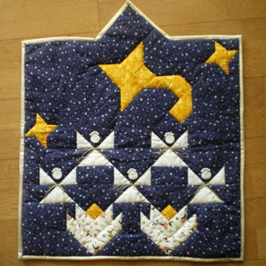 May include: A blue quilted wall hanging with a star design. The star is made of yellow fabric and is surrounded by smaller white stars. The background is a dark blue fabric with a white polka dot pattern.
