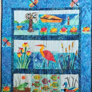 以下が含まれることがあります： 青と白のパッチワークのキルトで、ヘロン、ヤシの木、ガマ、魚など、自然をテーマにしたさまざまなデザインが施されています。キルトには、「ETANG」と書かれた看板と、いくつかの黄色の花も含まれています。