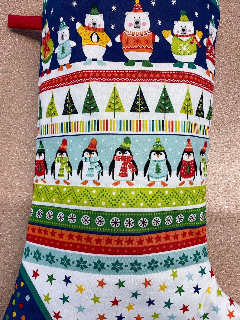 May include: A blue and white Christmas stocking with a red cuff. The stocking features a pattern of penguins, polar bears, and Christmas trees. The stocking is decorated with stars, snowflakes, and stripes.