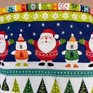May include: A blue and white fabric with a Christmas theme. The fabric features a repeating pattern of Santa Claus, polar bears, and Christmas trees. The fabric is ideal for crafting projects, such as making festive decorations, cushions, or quilts.