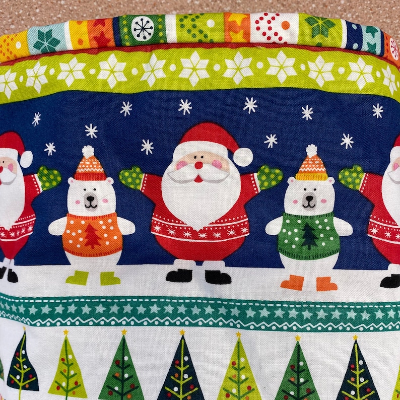 May include: A blue and white fabric with a Christmas theme. The fabric features a repeating pattern of Santa Claus, polar bears, and Christmas trees. The fabric is ideal for crafting projects, such as making festive decorations, cushions, or quilts.