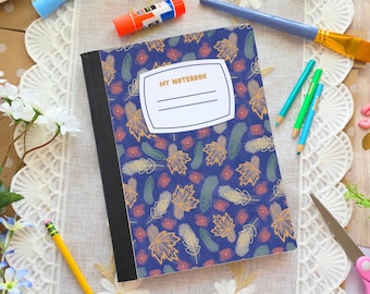May include: A composition notebook with a blue cover featuring a pattern of gold leaves, feathers, and red flowers. The notebook has a white label that reads "MY NOTEBOOK". Pencils, a paintbrush, and scissors are arranged around the notebook.