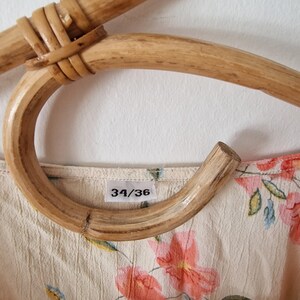 May include: A close-up of a white floral dress with a size tag that reads "34/36". The dress is hanging on a wooden hanger.