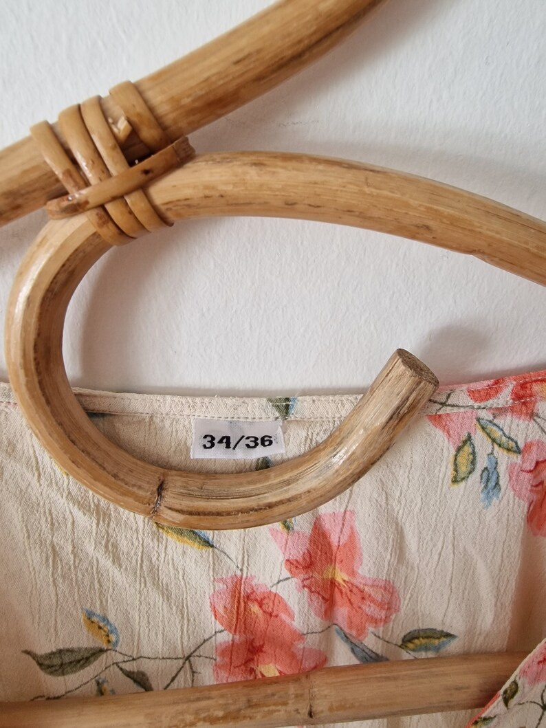 May include: A close-up of a white floral dress with a size tag that reads "34/36". The dress is hanging on a wooden hanger.