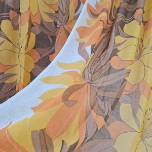Peut inclure: Gros plan sur un tissu à motifs floraux de grande taille dans les tons de jaune, orange et marron. Le motif présente des fleurs et des feuilles stylisées sur fond blanc. Le tissu est probablement utilisé pour l'habillement ou la décoration intérieure.
