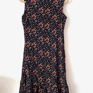 K&ouml;nnte beinhalten: Schwarzes &auml;rmelloses Kleid mit kleinem Blumenmuster in Orange-, Rot- und Lilat&ouml;nen. Das Kleid hat einen R&uuml;schen-Saum.