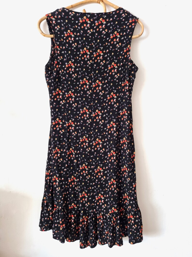 K&ouml;nnte beinhalten: Schwarzes &auml;rmelloses Kleid mit kleinem Blumenmuster in Orange-, Rot- und Lilat&ouml;nen. Das Kleid hat einen R&uuml;schen-Saum.