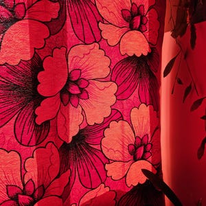 Può includere: Primo piano di un motivo floreale rosso. Il design presenta grandi fiori stilizzati in tonalità di rosso e corallo, con contorni neri. Il tessuto appare strutturato, creando un effetto audace e decorativo.