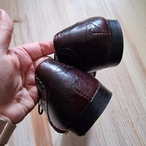 Pu&ograve; includere: Un paio di scarpe eleganti in pelle marrone scuro. Le scarpe presentano un design classico con perforazioni decorative e dettagli di cucitura. I tacchi sono neri e la pelle ha una finitura lucida.