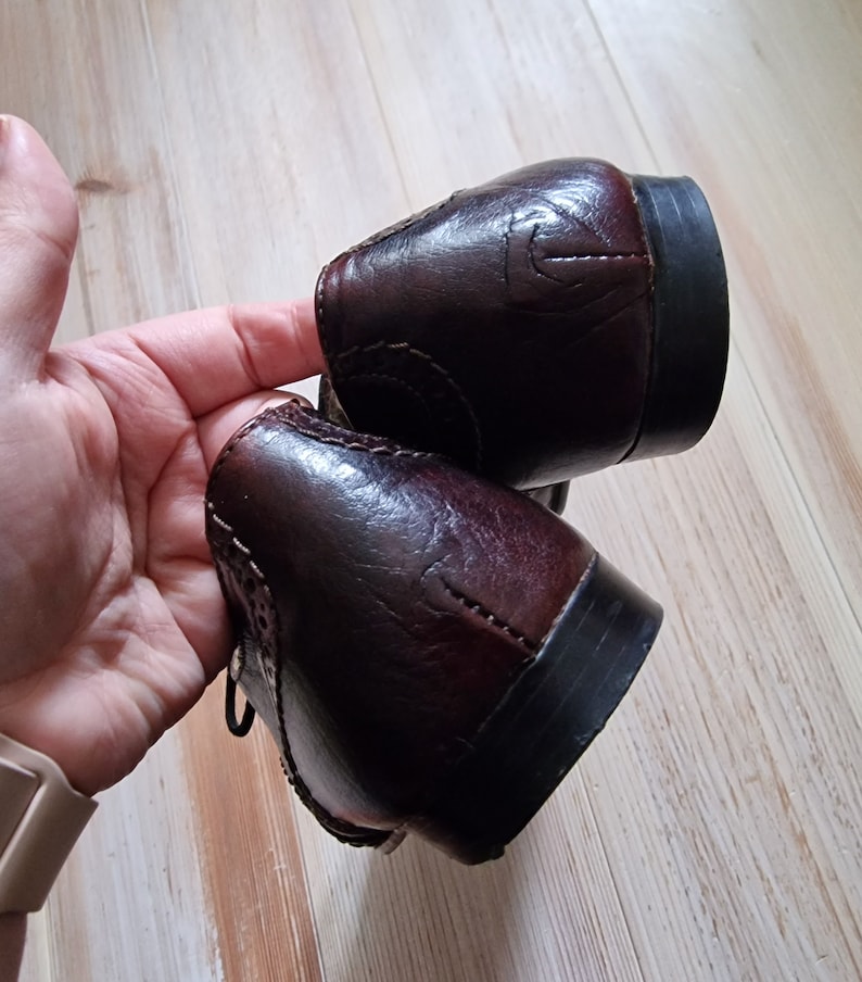Pu&ograve; includere: Un paio di scarpe eleganti in pelle marrone scuro. Le scarpe presentano un design classico con perforazioni decorative e dettagli di cucitura. I tacchi sono neri e la pelle ha una finitura lucida.