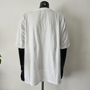 Op de afbeelding: Een effen wit T-shirt met korte mouwen, weergegeven op een zwarte mannequin. Het shirt heeft een ronde hals en een losse pasvorm. De stof lijkt een zacht, lichtgewicht materiaal te zijn.