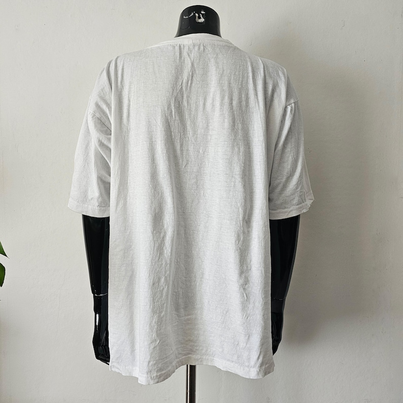 Op de afbeelding: Een effen wit T-shirt met korte mouwen, weergegeven op een zwarte mannequin. Het shirt heeft een ronde hals en een losse pasvorm. De stof lijkt een zacht, lichtgewicht materiaal te zijn.