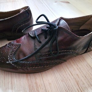 Pu&ograve; includere: Un paio di scarpe in pelle marrone con lacci neri. Le scarpe presentano perforazioni decorative e dettagli di cucitura. Lo stile &egrave; un classico design Oxford.