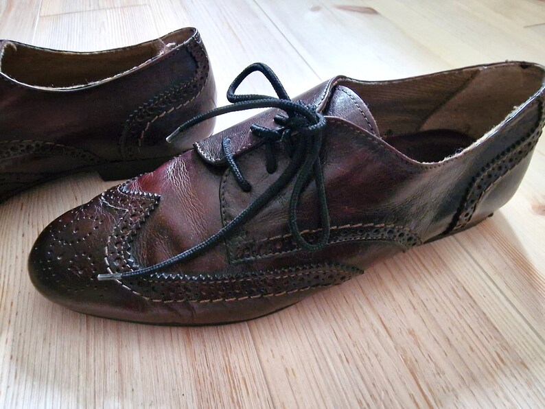 Pu&ograve; includere: Un paio di scarpe in pelle marrone con lacci neri. Le scarpe presentano perforazioni decorative e dettagli di cucitura. Lo stile &egrave; un classico design Oxford.