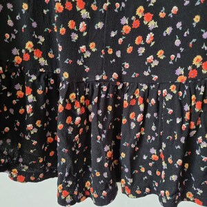 K&ouml;nnte beinhalten: Schwarzer Rock mit Blumenmuster mit kleinen roten, orangefarbenen, gelben und lila Bl&uuml;ten. Der Rock hat einen R&uuml;schen-Saum.
