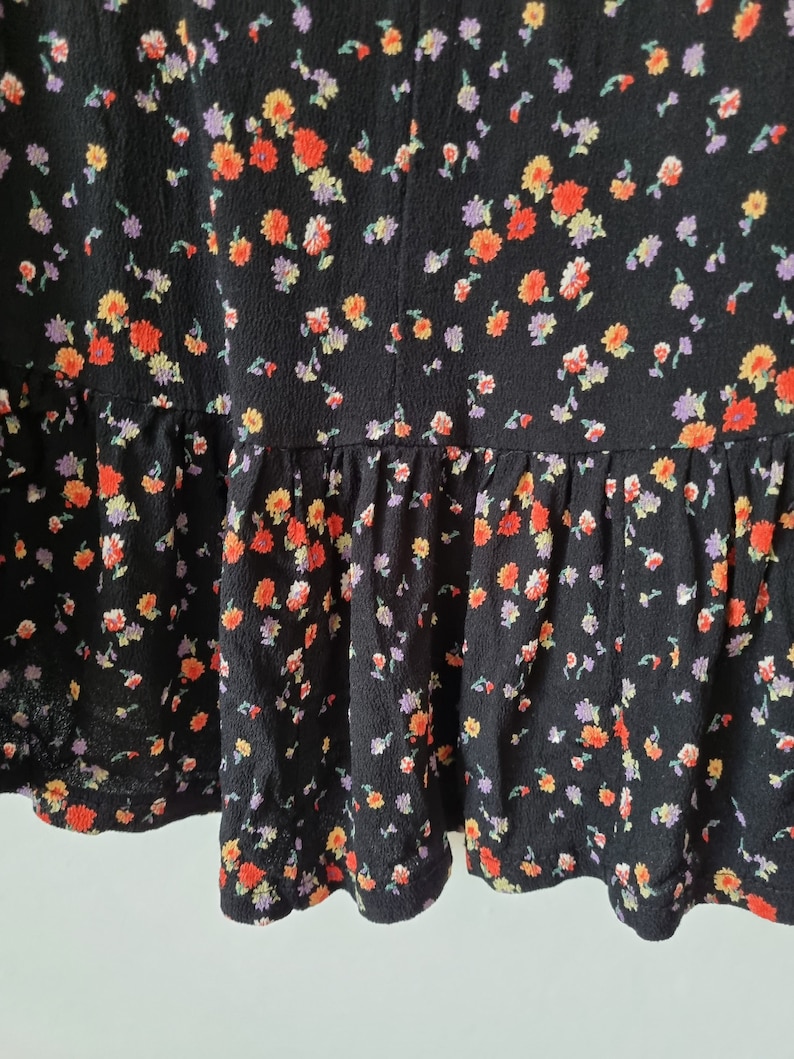 K&ouml;nnte beinhalten: Schwarzer Rock mit Blumenmuster mit kleinen roten, orangefarbenen, gelben und lila Bl&uuml;ten. Der Rock hat einen R&uuml;schen-Saum.