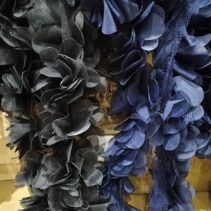 May include: Close-up of two decorative fabric garlands. One is a dark navy blue, the other a lighter blue. Both are made of layered, ruffled fabric, creating a floral or petal-like appearance. These garlands are likely for crafting or decoration purposes.