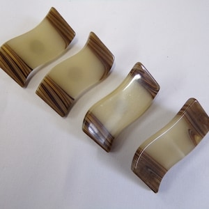 May include: Four chopstick rests made from a marbled material in shades of brown and cream. The rests are shaped like a gentle curve.