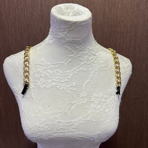 May include: Gold chain strap with black adjustable ends. The strap is displayed on a white mannequin.