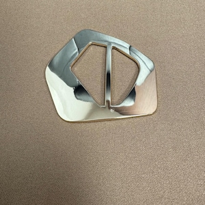 Może przedstawiać: Złota metalowa klamra o prostokątnym kształcie i gładkim, polerowanym wykończeniu.