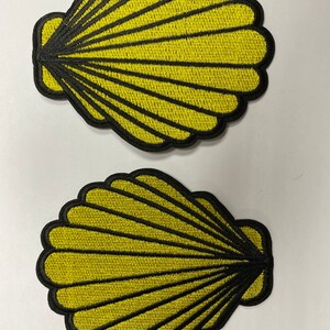 May include: Two yellow embroidered fabric patches shaped like seashells. The shells have a black outline and are about 6 inches wide.