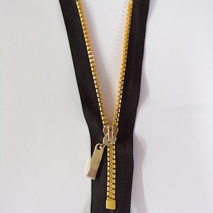May include: A black zipper with gold teeth and a silver pull tab. The zipper is open and the teeth are visible.