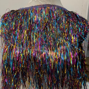 May include: A multi-coloured metallic fringe trim with a blue, gold, pink, and purple colour scheme. The fringe is approximately 5 cm long and is perfect for adding a touch of sparkle to any project.