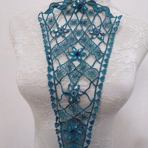 May include: Teal crochet lace collar with a geometric pattern and embellished with iridescent rhinestones. The collar is displayed on a white lace-covered mannequin.