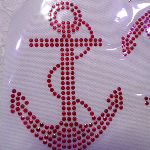 May include: A red anchor design made of rhinestones on a white fabric background.
